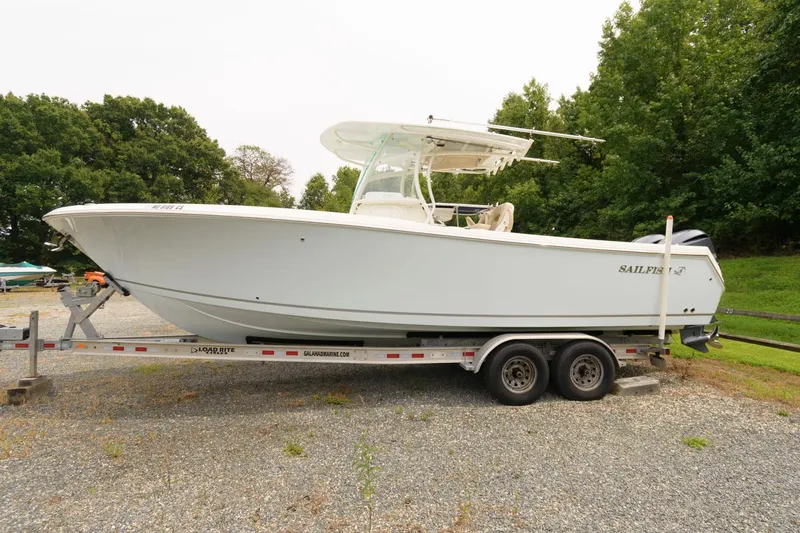 Slide: The Image of 2018 Sailfish 290 CC boat on a trailer in a gravel lot with trees in the background. - 1