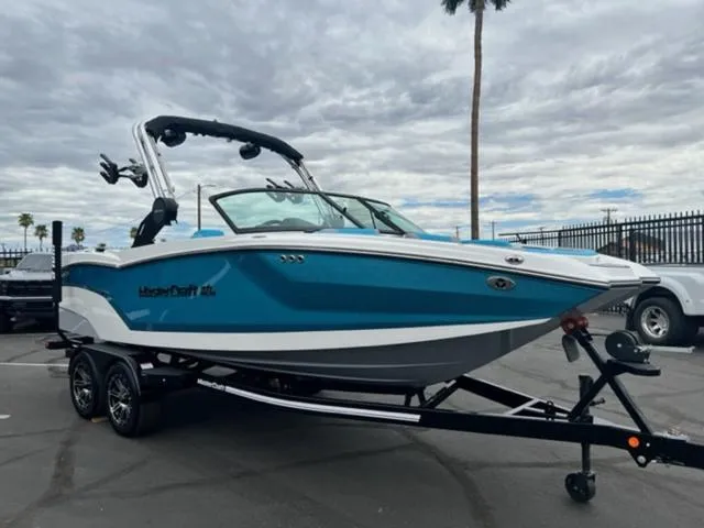 Slide: The Image of 2023 MasterCraft NXT22 boat in vibrant blue on a trailer, parked outdoors. - 4