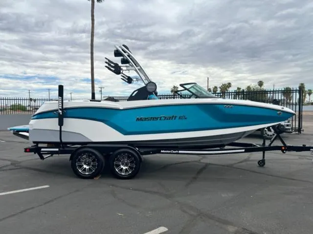 Slide: The Image of 2023 MasterCraft NXT22 boat on trailer, blue and white design, parked outdoors. - 5