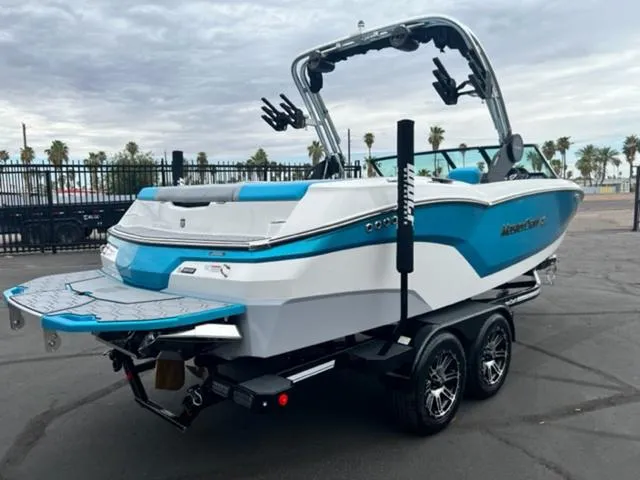 Slide: The Image of 2023 MasterCraft NXT22 boat, blue and white, on a trailer in a parking lot. - 6