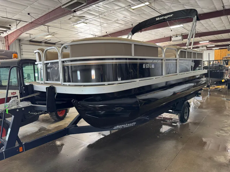 Slide: The Image of 2021 Ranger 200C pontoon boat in a warehouse, on a trailer, with a black canopy. - 1