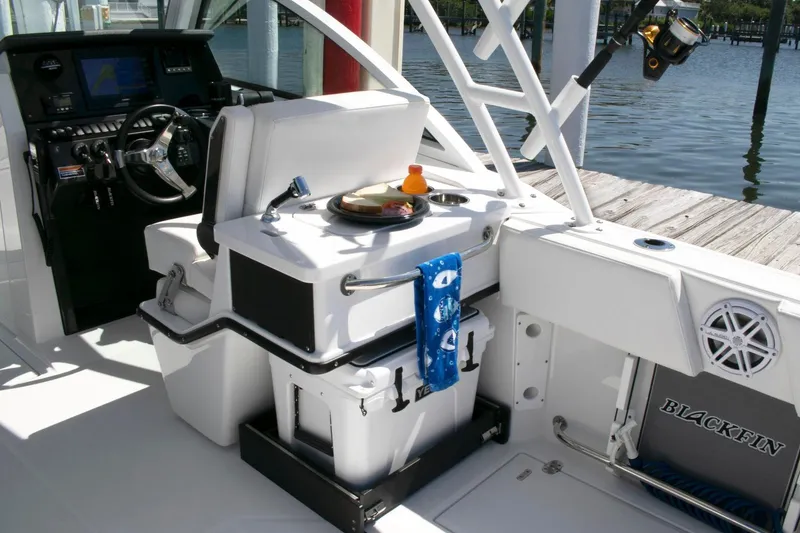 Slide: The Image of 2024 Blackfin 252DC boat interior with helm, seating, and fishing gear by the dock. - 11