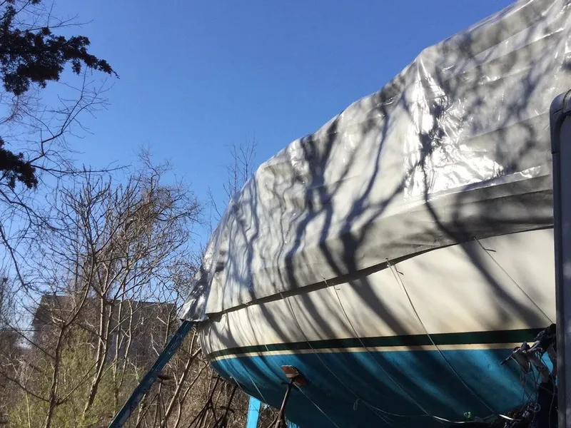 Slide: The Image of 1977 Gulfstar 37 sailboat covered with tarp, surrounded by trees under clear blue sky. - 17