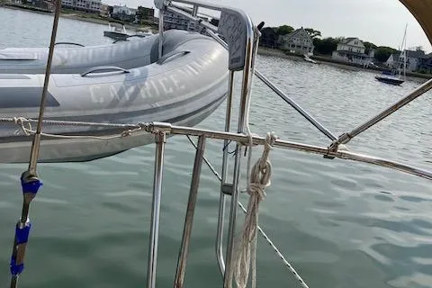 Slide: The Image of 1977 Gulfstar 37 sailboat with dinghy on calm water, coastal houses in background. - 5