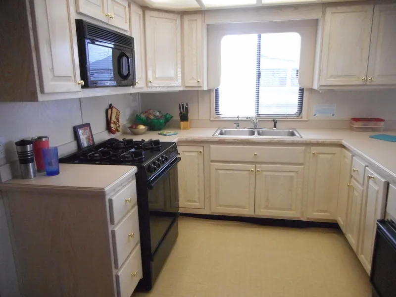 Slide: The Image of 1995 Stardust Cruisers The Verdict houseboat kitchen with white cabinets and black appliances. - 28