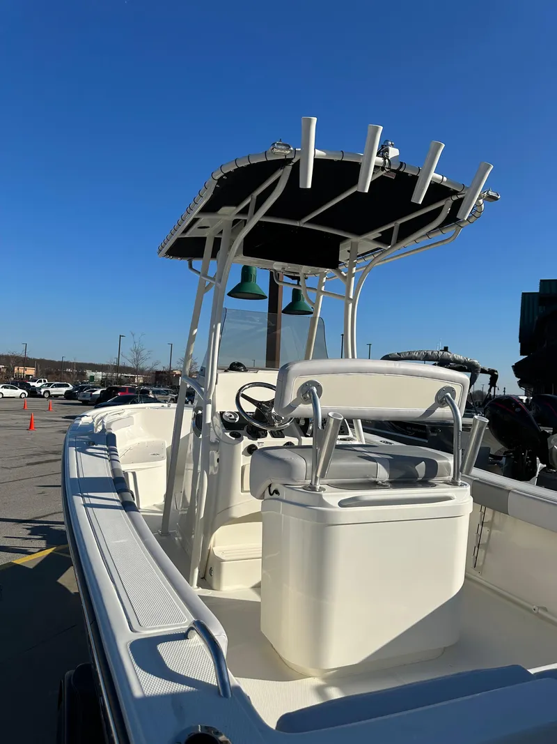 Slide: The Image of 2024 Mako 214 CC boat with T-top and rod holders, parked outdoors. - 4