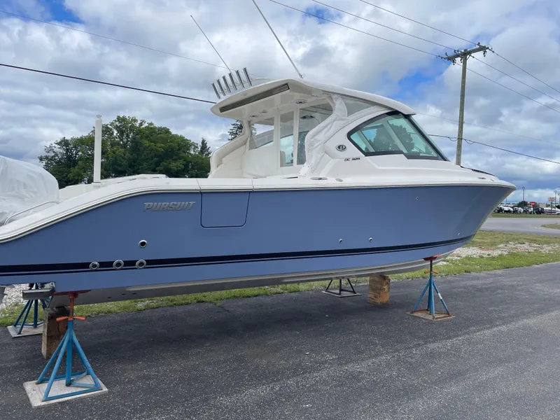 Slide: The Image of 2024 Pursuit DC 326 Dual Console boat on stands, blue hull, outdoor display. - 2