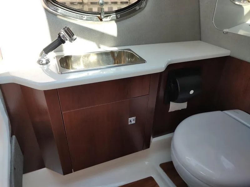 Slide: The Image of 2018 Chaparral 267 SSX boat bathroom with sink, toilet, and wooden cabinetry. - 24