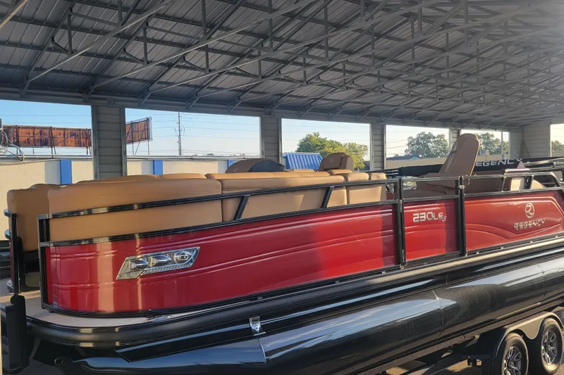 The Image of 2024 Regency 230 LE3 Sport pontoon boat with red exterior under a metal roof. - 0