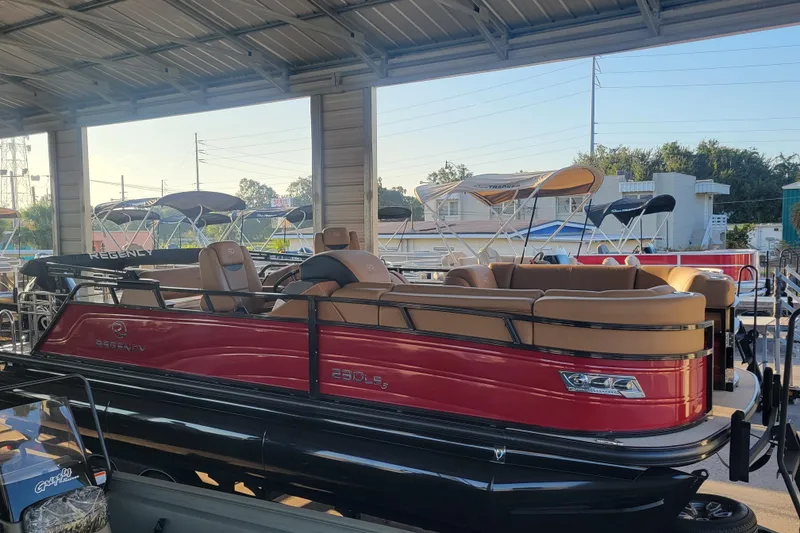 Slide: The Image of 2024 Regency 230 LE3 Sport pontoon boat in showroom, featuring sleek red and tan design. - 1
