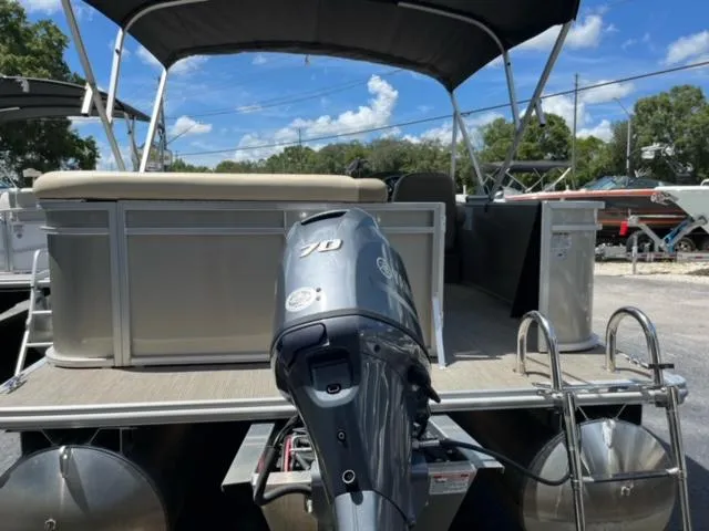 Slide: The Image of 2024 SunChaser Geneva Cruise 20 pontoon boat with outboard motor, docked under blue sky. - 14