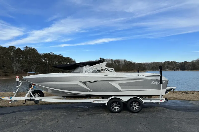 Slide: The Image of 2024 Tigé RZX22 boat on trailer by a lake with a clear blue sky. - 0