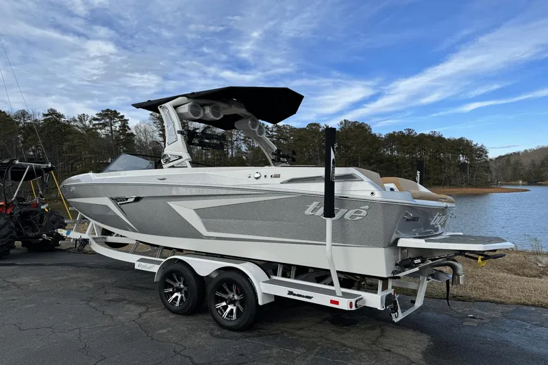 Slide: The Image of 2024 Tigé RZX22 boat on trailer by a lake, ready for water sports. - 2