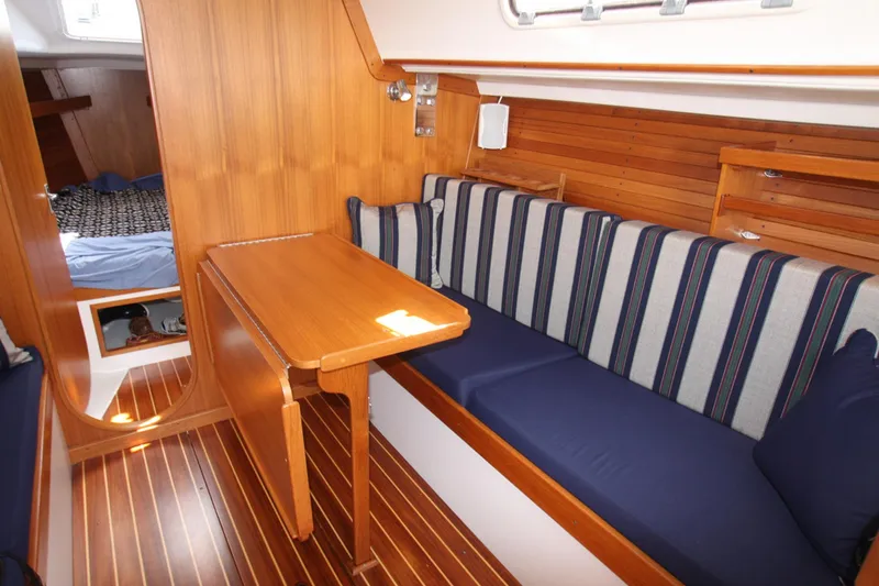 Slide: The Image of Interior of 2001 J Boats 32, featuring wooden table, striped seating, and cozy cabin. - 32