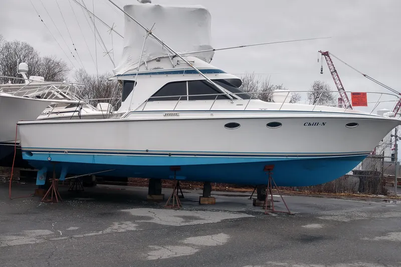 Slide: The Image of 1988 Trojan 12 Meter boat on stands, white hull with blue bottom, covered cockpit. - 2