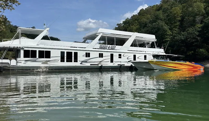 Slide: The Image of 2003 Outerlimits 42 GTX speedboat docked beside a large white houseboat on a calm lake. - 14