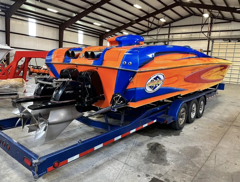 Slide: The Image of 2003 Outerlimits 42 GTX powerboat in vibrant orange and blue, on a triple-axle trailer in a warehouse. - 2