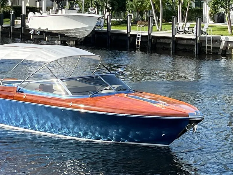 Slide: The Image of 2012 Riva Aquariva Super boat with blue hull and wooden deck on a calm waterway. - 1