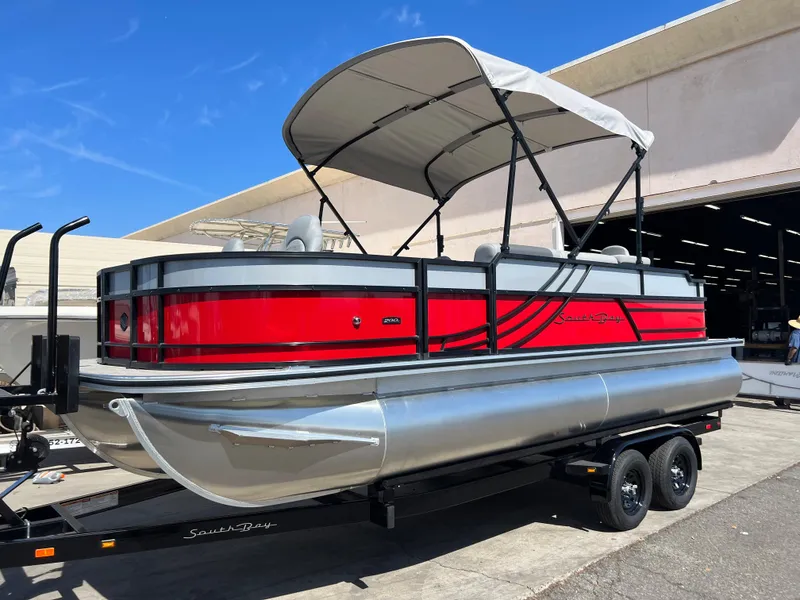 Slide: The Image of 2023 South Bay 22F 200 Series pontoon boat with red and silver design on trailer. - 2