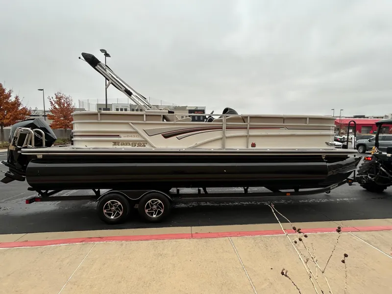 Slide: The Image of 2023 Ranger Reata 243C pontoon boat on a trailer in a parking lot. - 1