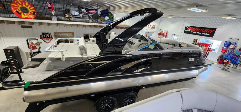 Slide: The Image of 2024 Bennington 25QXSBA pontoon boat in showroom, black exterior, luxury seating. - 16