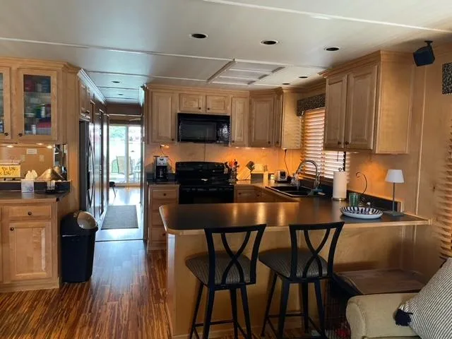 Slide: The Image of 2006 Sumerset Houseboat kitchen with wooden cabinets, black appliances, and bar seating. - 10