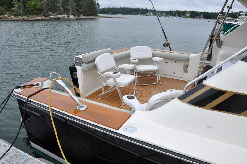 Slide: The Image of 1987 Bertram 37 Convertible boat with fishing chairs on deck, docked by a scenic lake. - 8