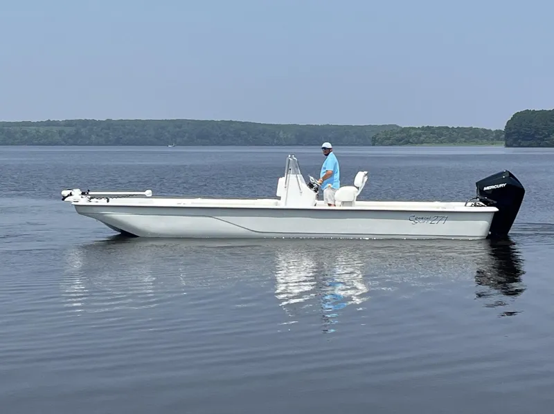 Slide: The Image of 2024 Coastal Skiff 271 boat on calm water with a person standing at the helm. - 13