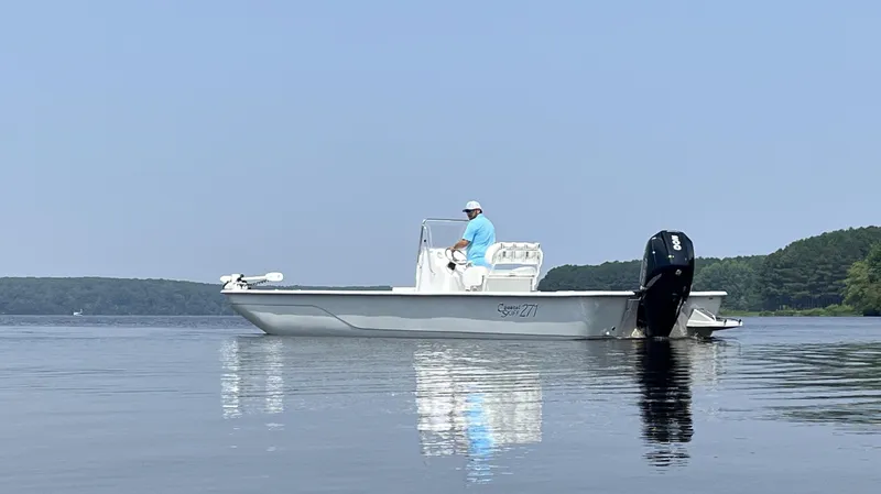 Slide: The Image of 2024 Coastal Skiff 271 boat on calm water with a person at the helm. - 14