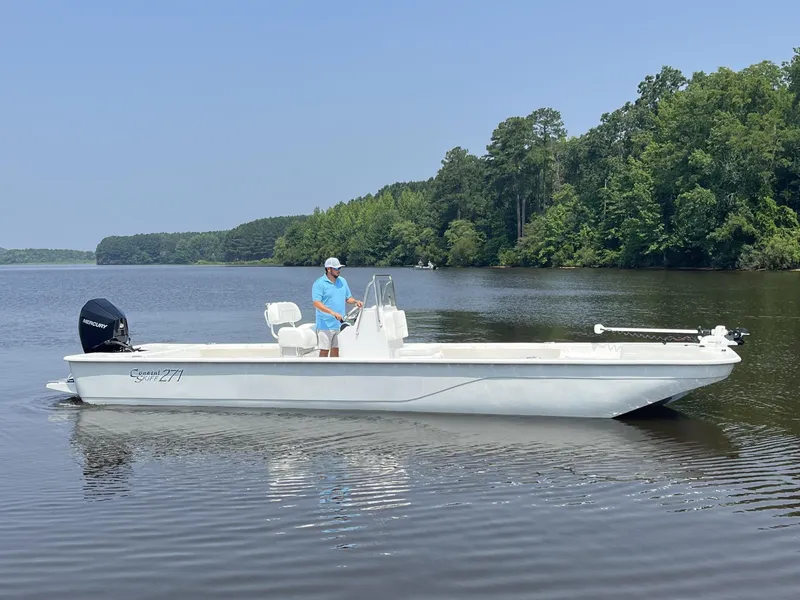 Slide: The Image of 2024 Coastal Skiff 271 boat on a calm lake with a person at the helm. - 16