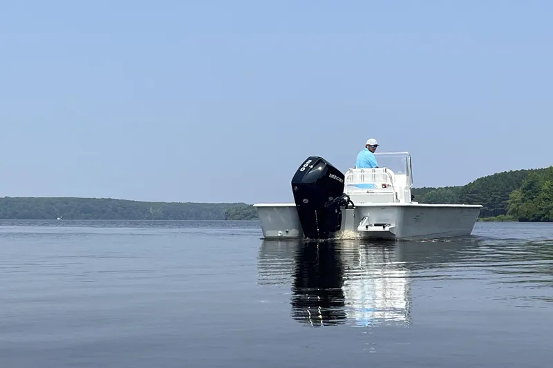 Slide: The Image of 2024 Coastal Skiff 271 boat on calm water with a person at the helm. - 19
