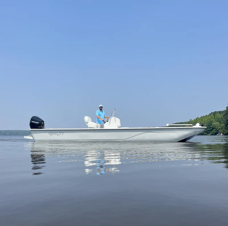 Slide: The Image of 2024 Coastal Skiff 271 boat on calm water with a person at the helm. - 21