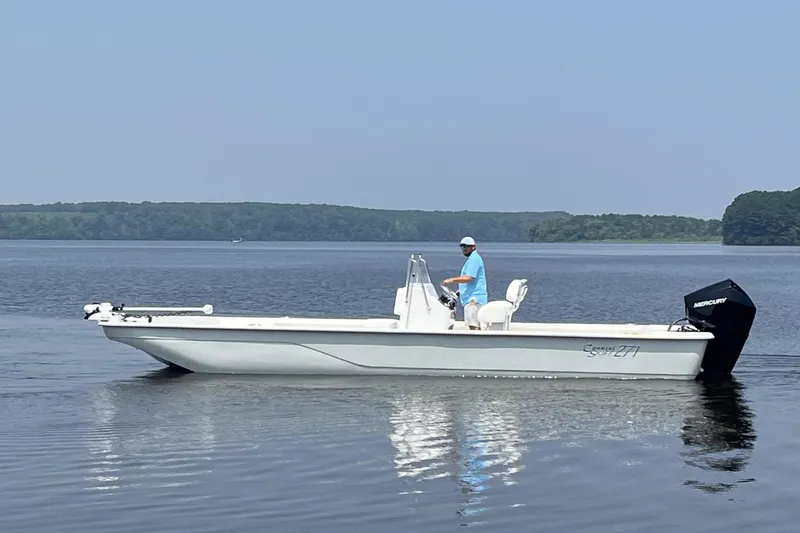 Slide: The Image of 2024 Coastal Skiff 271 boat on calm water with a person at the helm. - 25