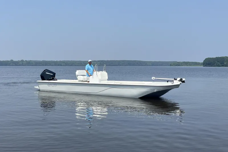 Slide: The Image of 2024 Coastal Skiff 271 boat on calm water with a person standing at the helm. - 26