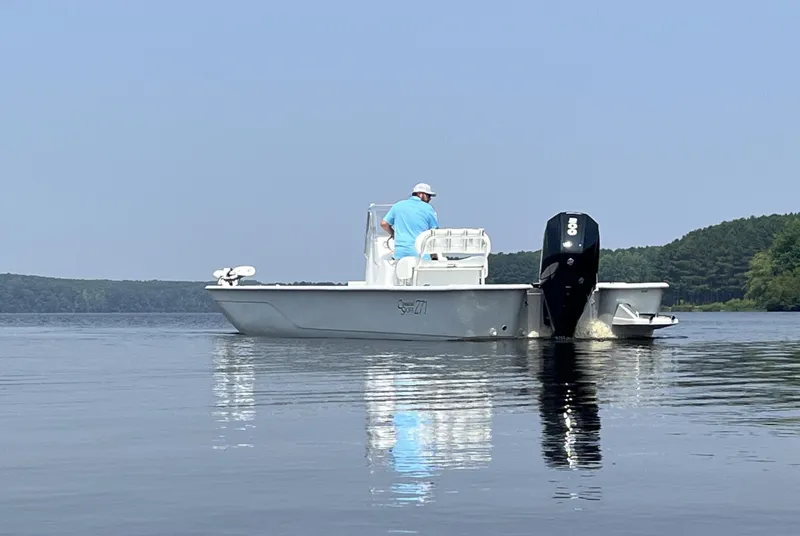 Slide: The Image of 2024 Coastal Skiff 271 boat on calm water with a person at the helm. - 27