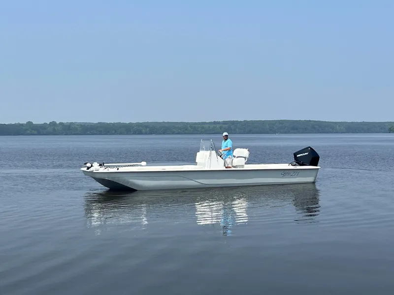 Slide: The Image of 2024 Coastal Skiff 271 boat on calm water with a person standing. - 28