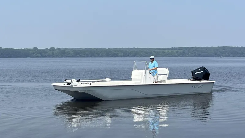 Slide: The Image of 2024 Coastal Skiff 271 boat on calm water with a person at the helm. - 29