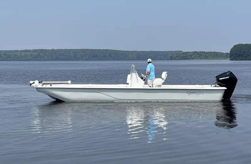 Slide: The Image of 2024 Coastal Skiff 271 boat on calm water with a person standing. - 3