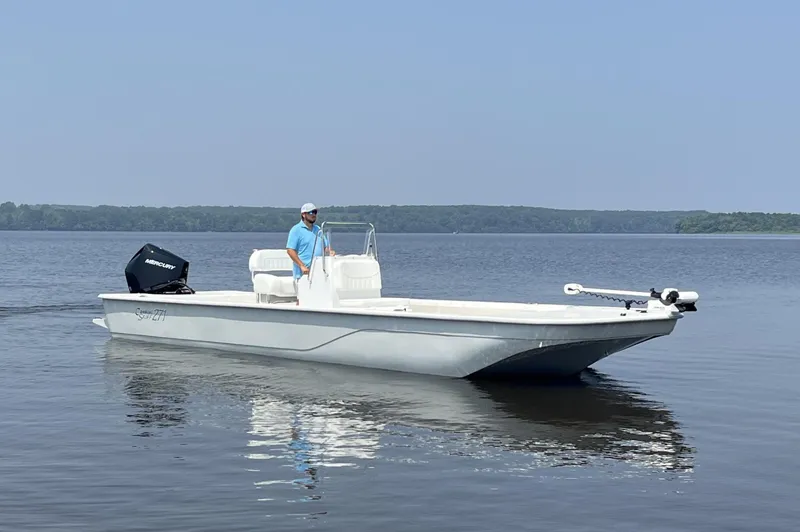 Slide: The Image of 2024 Coastal Skiff 271 boat on calm water with a person at the helm. - 31