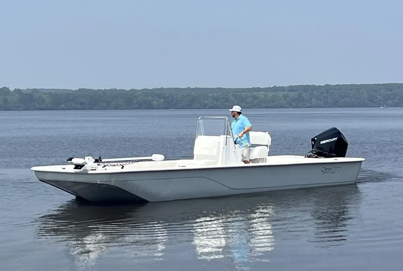 Slide: The Image of 2024 Coastal Skiff 271 boat on calm water with a person at the helm. - 33
