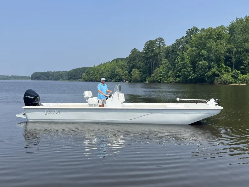 Slide: The Image of 2024 Coastal Skiff 271 boat on a calm lake with a person at the helm. - 36