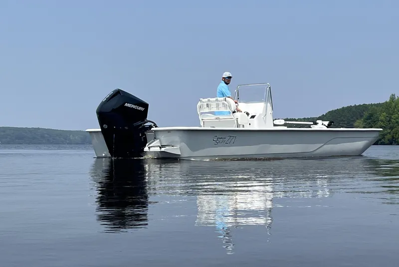 Slide: The Image of 2024 Coastal Skiff 271 boat on calm water with a Mercury outboard motor. - 4