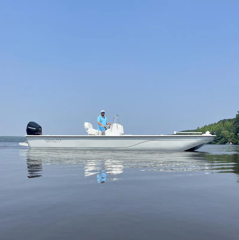 Slide: The Image of 2024 Coastal Skiff 271 boat on calm water with a clear blue sky. - 8