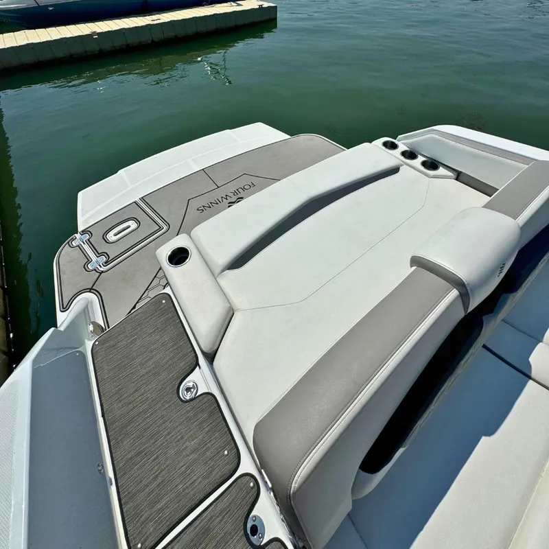 Slide: The Image of 2021 Four Winns HD8 boat interior with cushioned seating, docked near a modern building. - 10