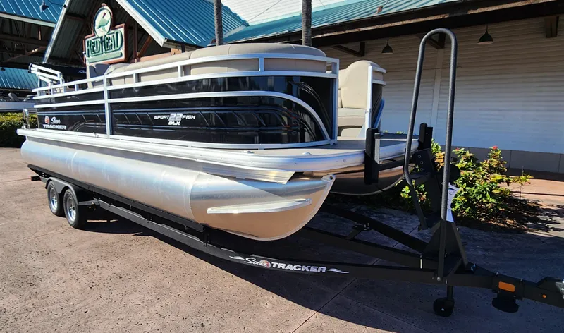 Slide: The Image of 2024 Sun Tracker SportFish 22 DLX pontoon boat on a trailer outside a building. - 2