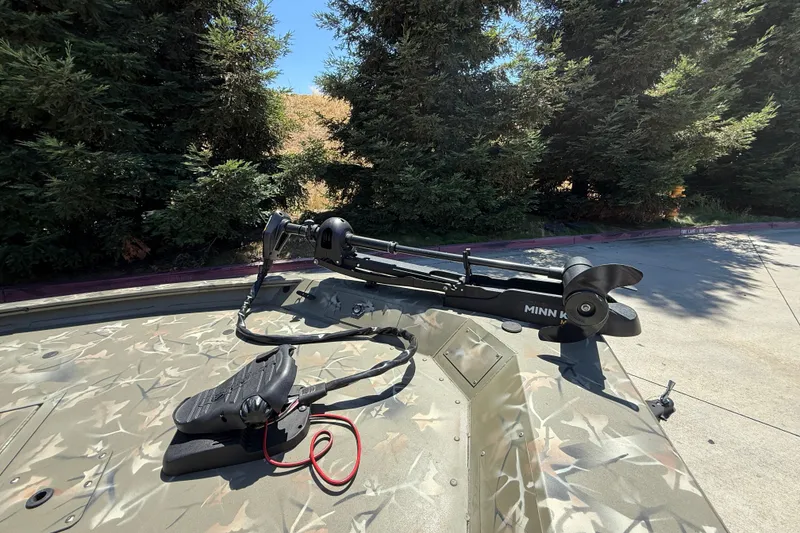 Slide: The Image of 2024 Tracker Grizzly 1754 SC boat with Minn Kota trolling motor in a wooded area. - 6