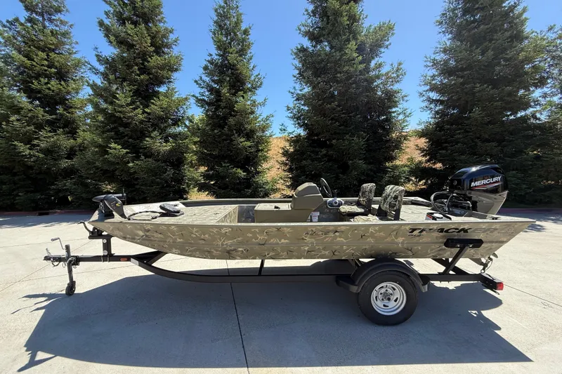 The Image of 2024 Tracker Grizzly 1754 SC boat on trailer, parked outdoors with trees in background. - 0