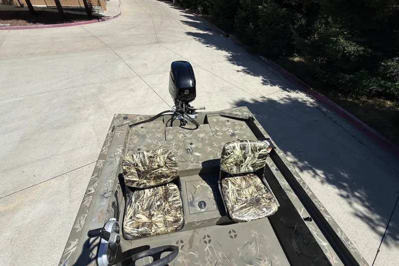 Slide: The Image of 2024 Tracker Grizzly 1754 SC boat with camouflage seats and motor, parked on concrete. - 9