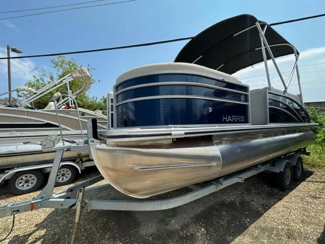 Slide: The Image of 2023 Harris 210 Cruiser pontoon boat on a trailer under a clear blue sky. - 2