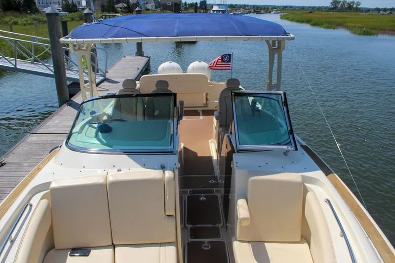 Slide: The Image of 2017 Chris-Craft Calypso 30 boat with blue canopy docked on a serene waterway. - 2